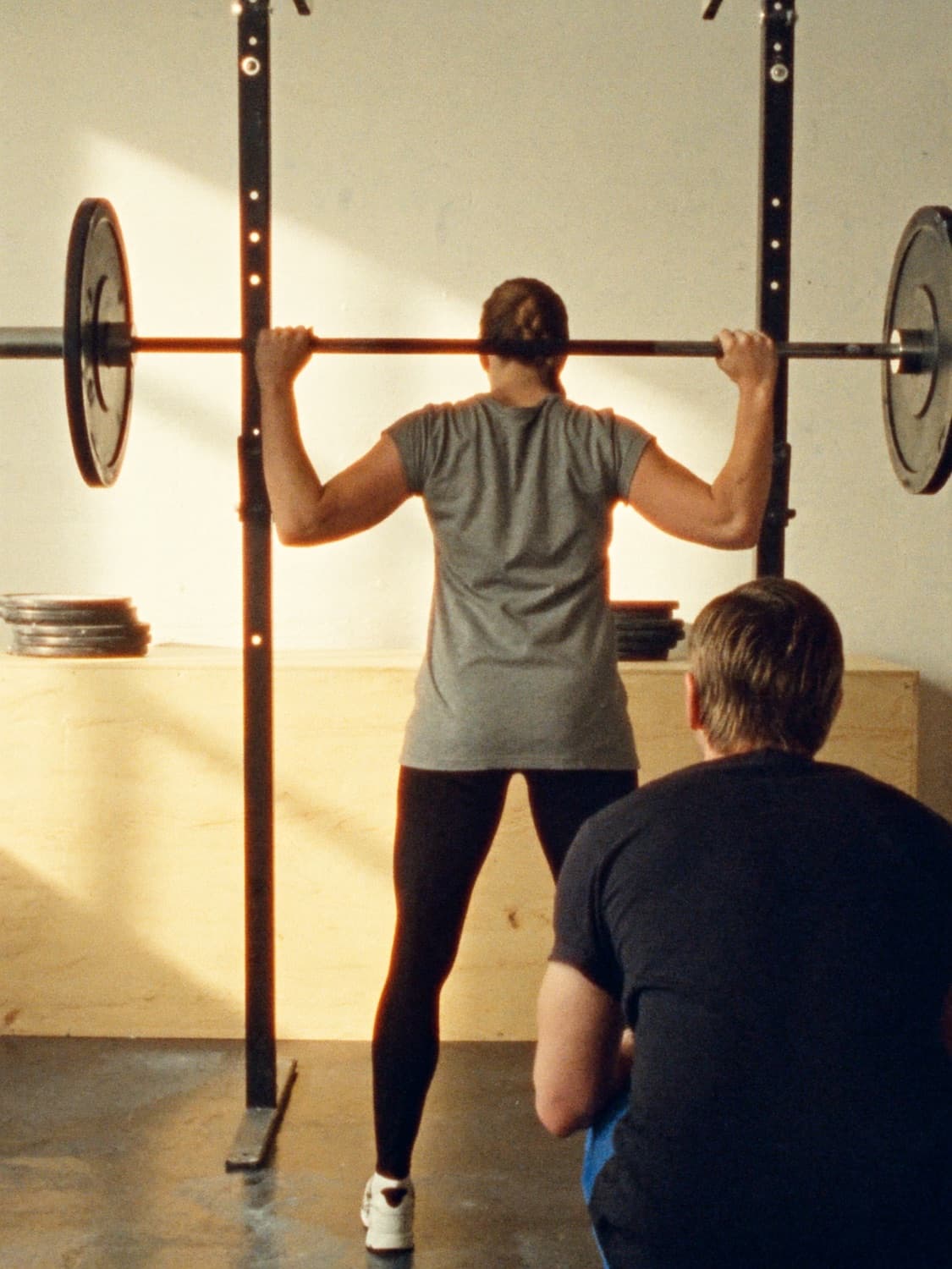 A personal trainer watching a client train in a bright gym