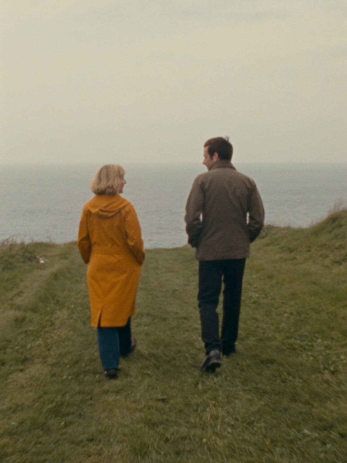 Two people walking and talking along a clifftop path above the sea