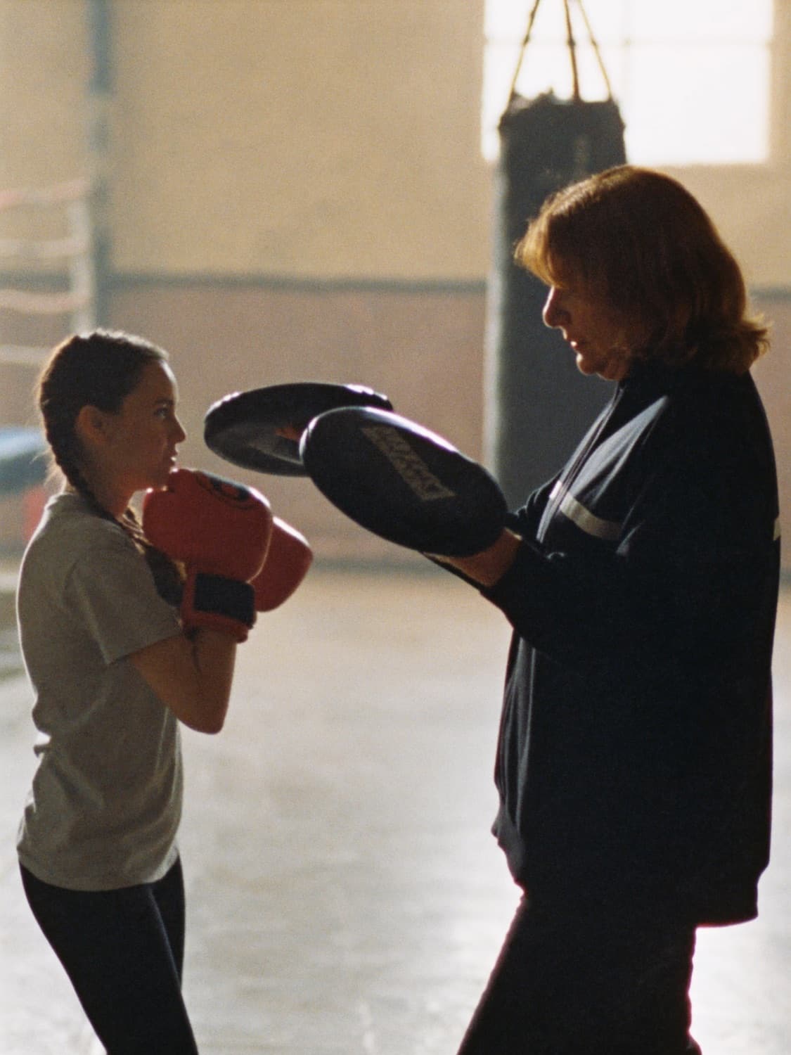 A boxing coach holding pads for a young boxer in a community gym