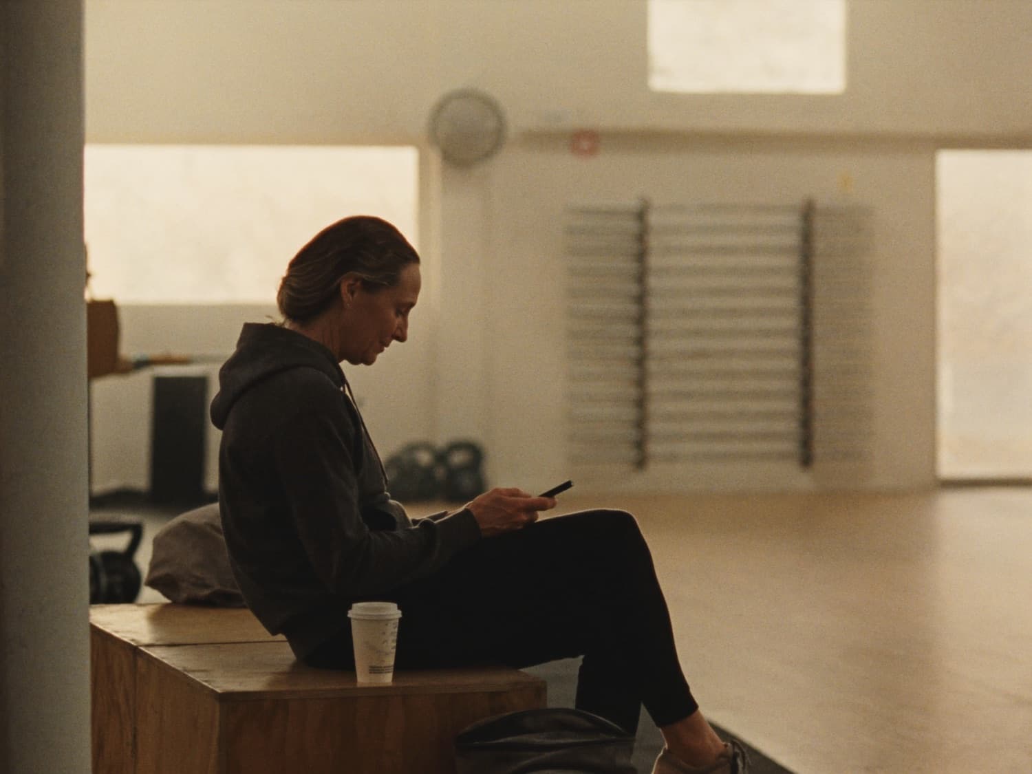 A coach reading a message on her phone in an empty gym before her first client