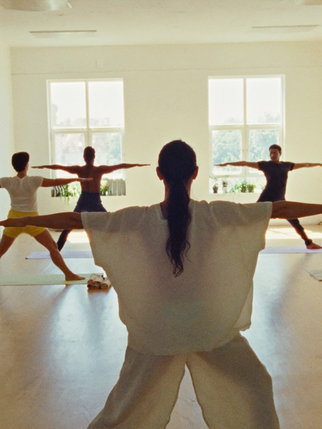 A yoga teacher leading a small class in a sunlit studio